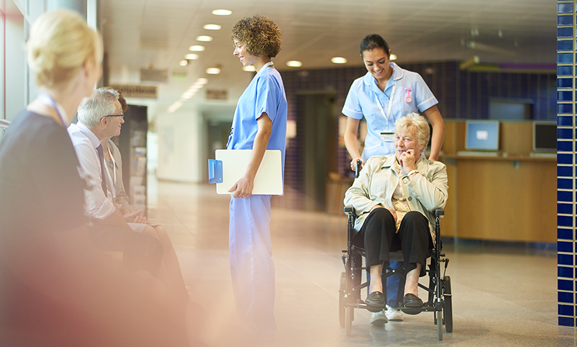 Zorgprofessional in de hal van een ziekenhuis met dame in een rolstoel