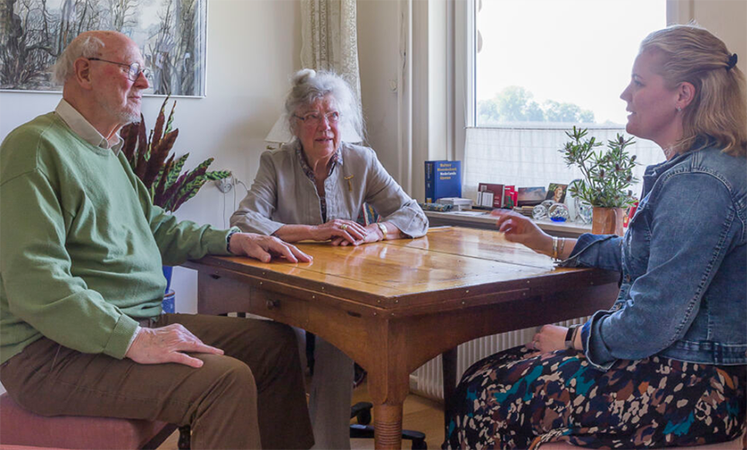 Zorgprofessional praat met ouder echtpaar in huis