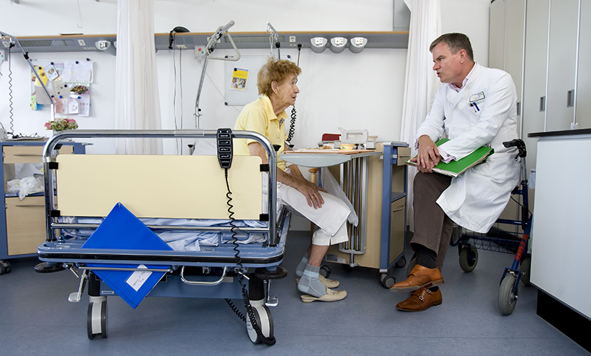 Zorgprofessional in gesprek met patiënt op ziekenhuisbed