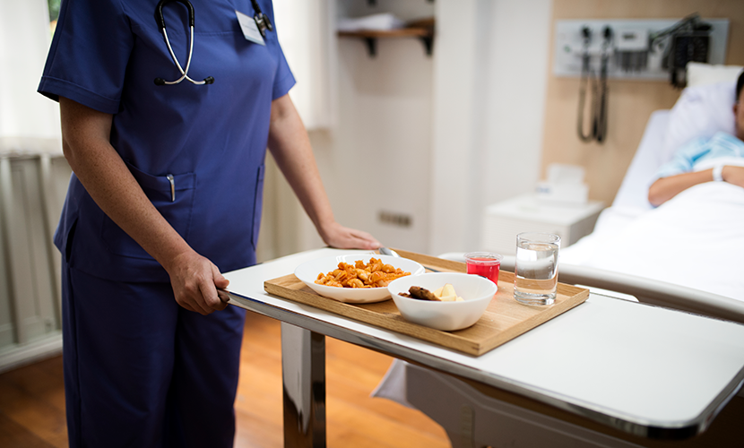 Zorgprofessional brengt blad met eten naar patiënt