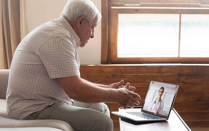 Oudere man zit voor laptop en praat met zorgprofessional